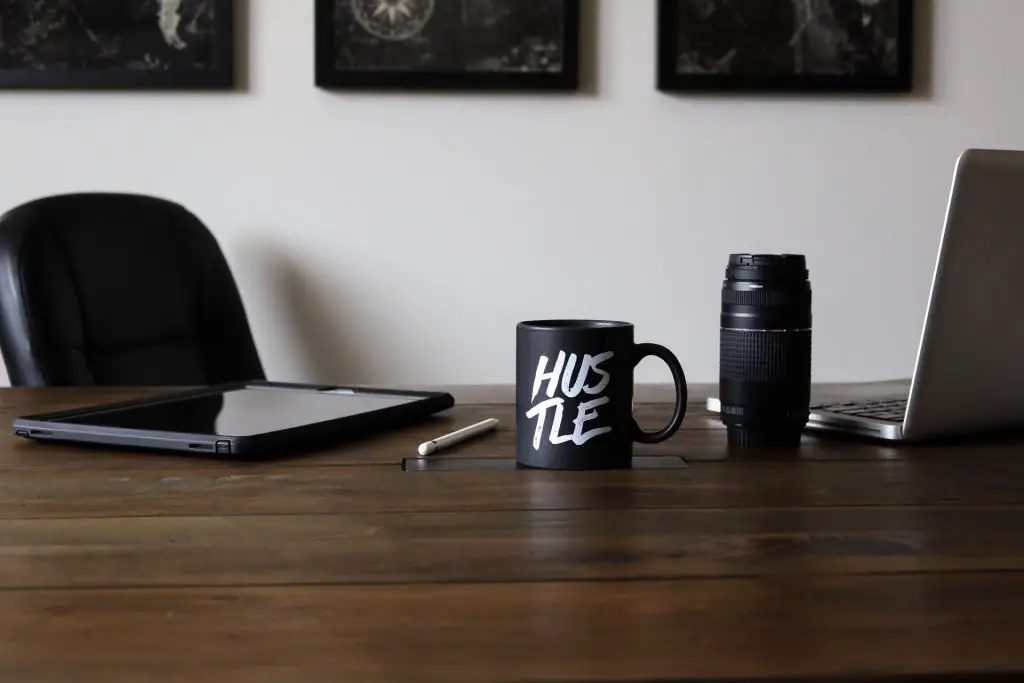 Hustle coffee mug next to camera lens and laptop